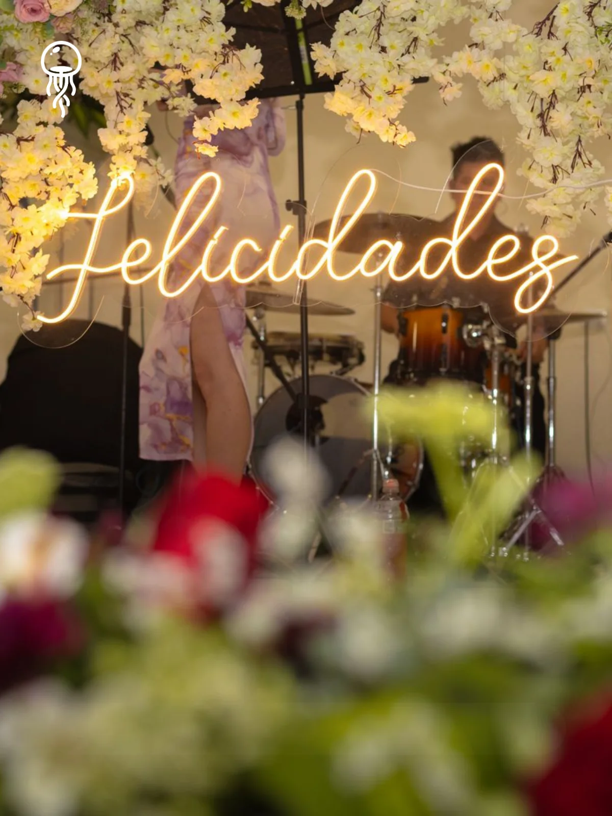 Salones Aurora: letrero de neón «Felicidades» entre flores, con la banda al fondo